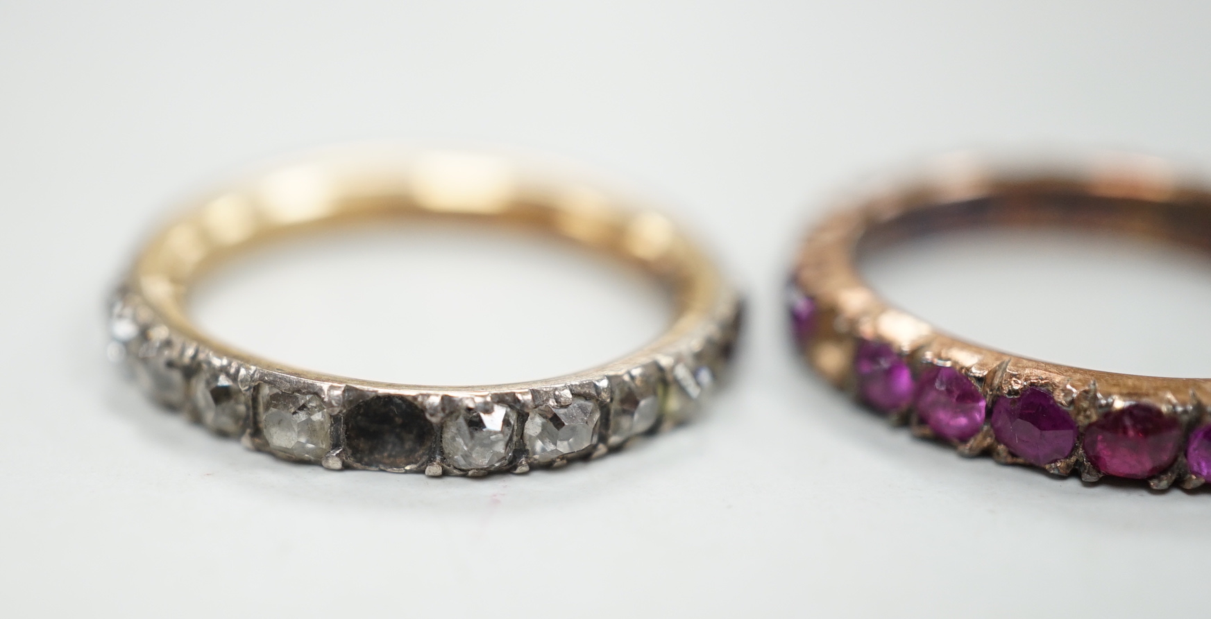 An antique yellow metal and diamond set full eternity ring (stone missing), size L and a similar pink stone set eternity ring.